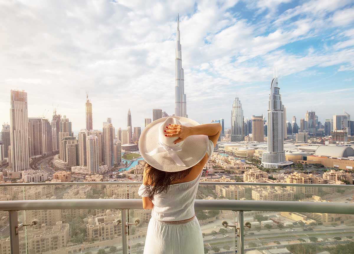 Woman with a white hat is standing on a balcony in front of dubai skyline