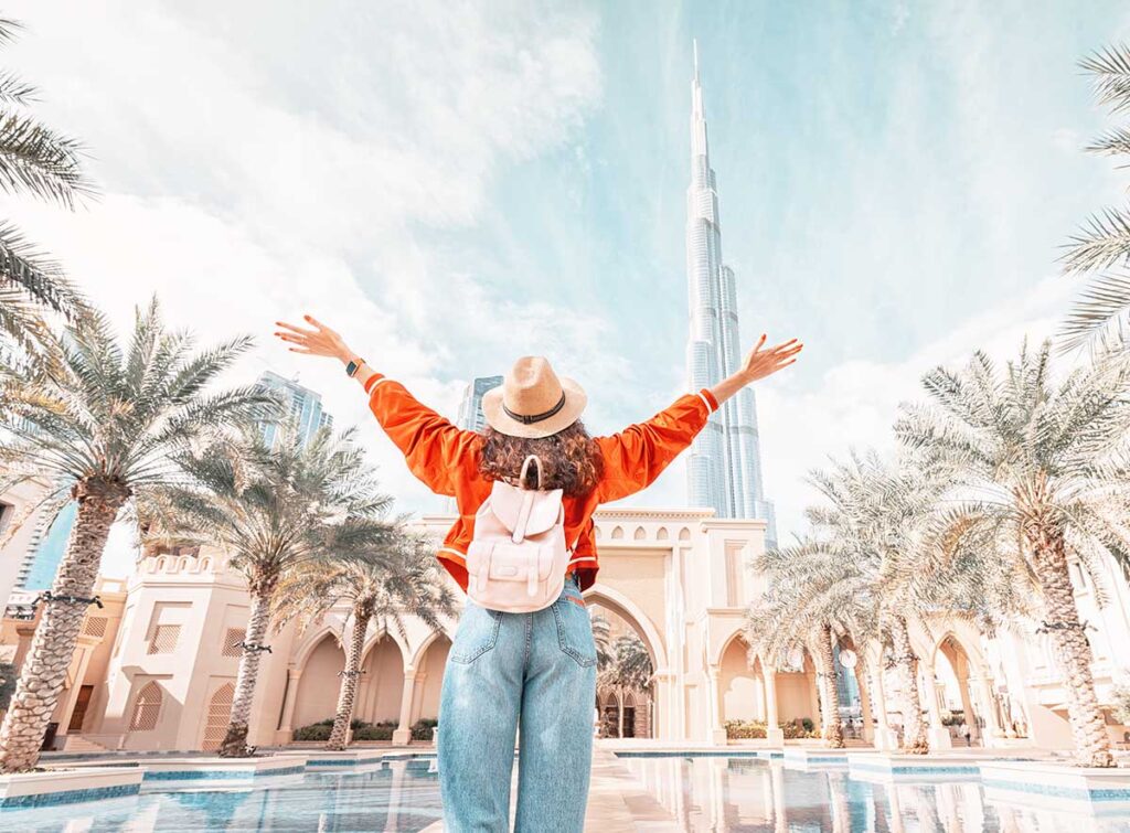 From behind, you can see the traveler girl arms spread wide as she take in the incredible view of the Burj Khalifa and the Dubai skyline.