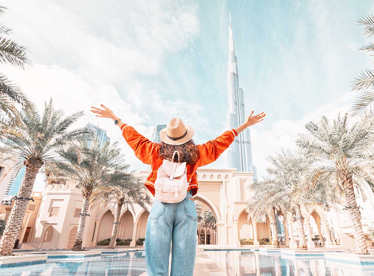 From behind, you can see the traveler girl arms spread wide as she take in the incredible view of the Burj Khalifa and the Dubai skyline.